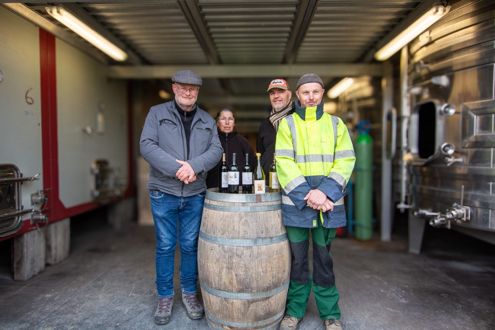 Photo d'Ingo, Jérôme, Solange travailleurs de l'atelier viticole en photo avec Benoit leur moniteur dans le chais de production autours d'une barrique présentant la gamme de vin.