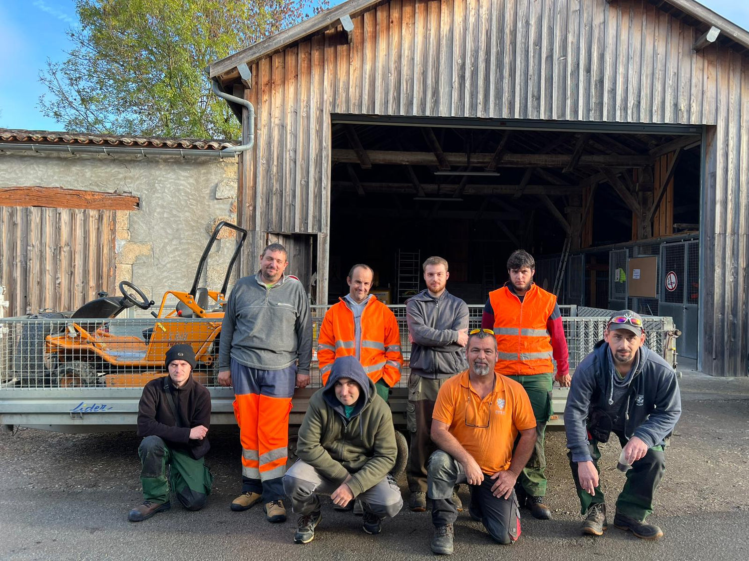 Equipe des espaces verts pris en photo de bon matin ensoleillé avec leur moniteur devant leur atelier et camions prêts à partir chez des clients. 